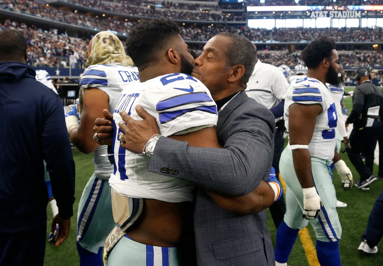 Dallas Cowboys running back Ezekiel Elliott embraces Hall of Famer Tony Dorsett as the two chat on the sideline in the first half of an NFL football game against the Baltimore Ravens on Sunday, Nov. 20, 2016, in Arlington, Texas. (AP Photo/Michael Ainsworth)