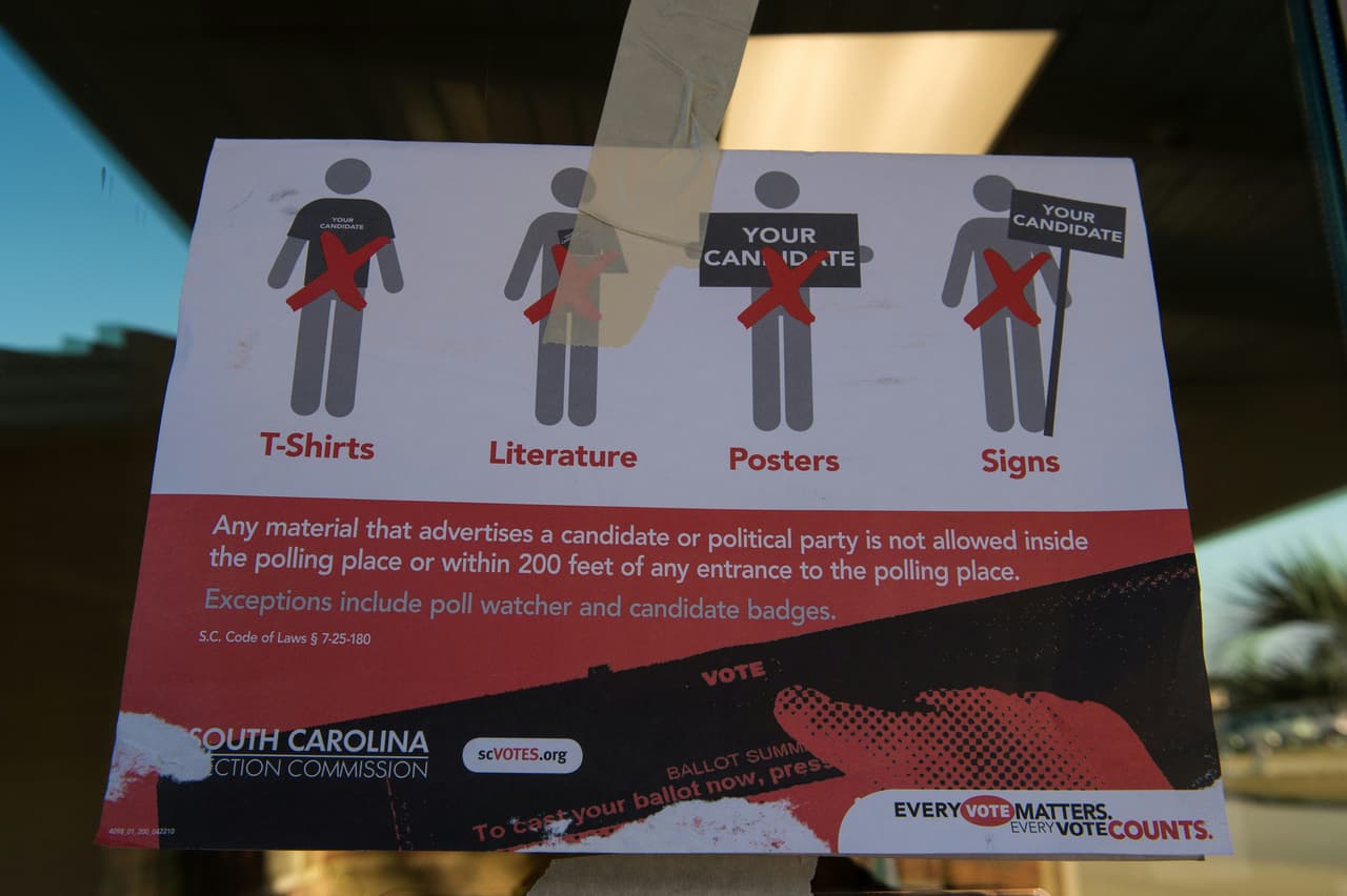 Este cartel prohíbe a las personas acudir a votar portando algo que muestre abiertamente el apoyo a alguno de los candidatos. (Foto por Nicholas Kamm, AFP).