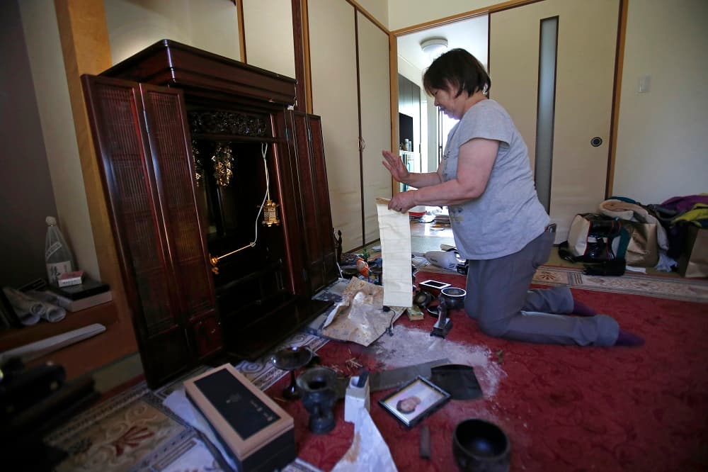 Una mujer limpia el altar budista de su madre, afectado por el terremoto de 6.5 que sacudió Japón el jueves