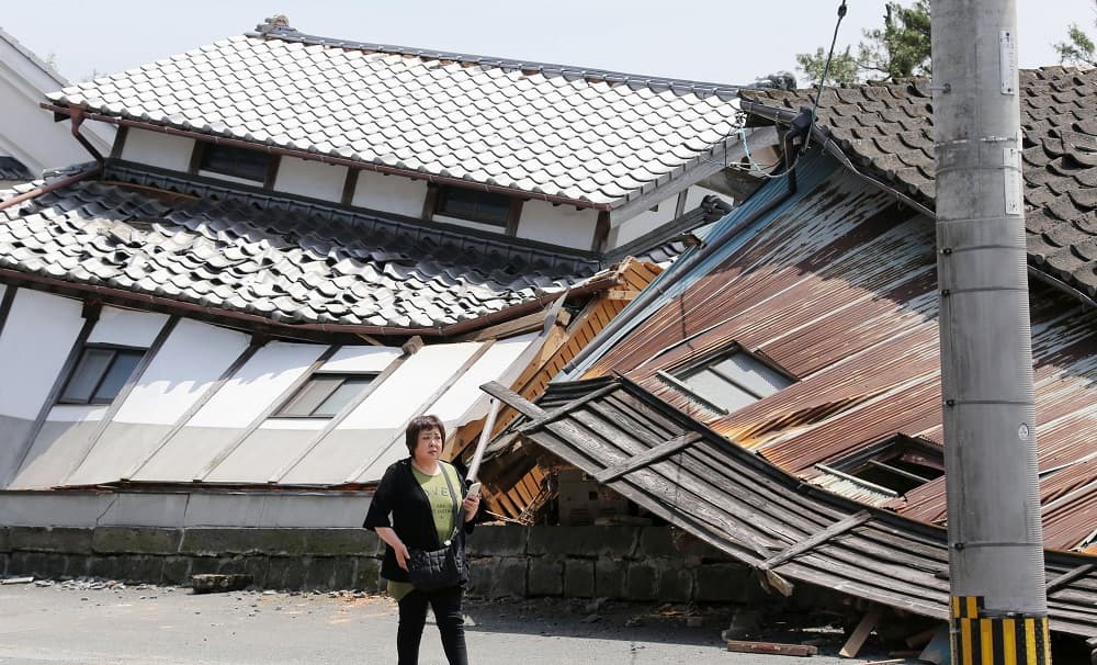 Una mujer pasa por delante de viviendas destruidas por un sismo de 6.5 grados registrado el jueves en Mashiki, en la prefectura de Kumamoto