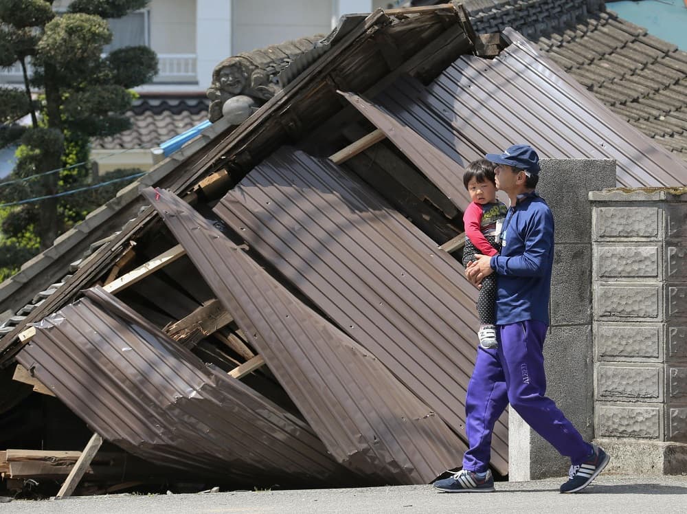 Un hombre pasea junto con un menor frente a algunos de los edificios colapsados en la ciudad de Mashiki