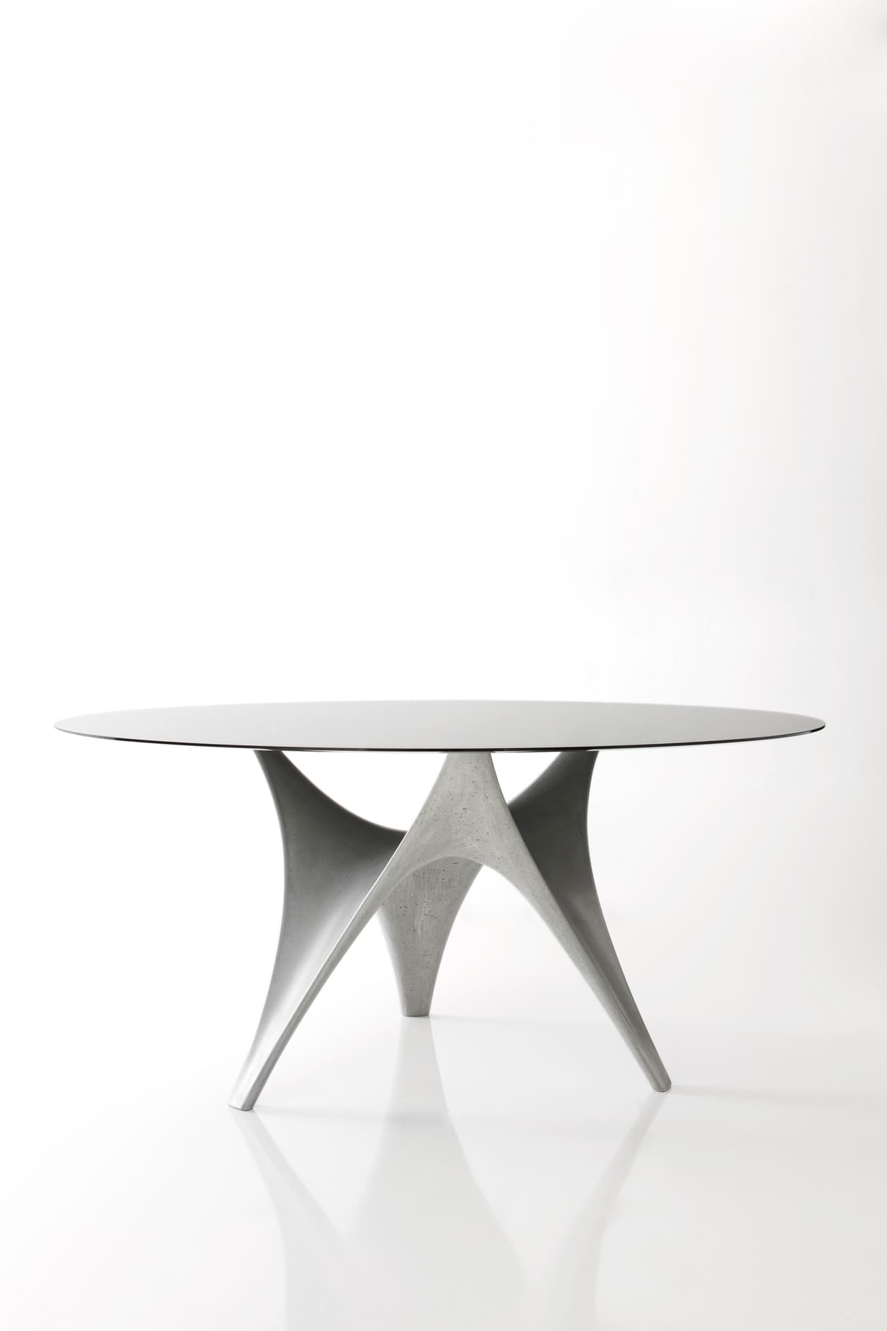 Mesa Arc -- Diseñada en 2010 para Molteni & C (molteni.it), la base, que es producto directo de las herramientas digitales, se fabrica en Ductal, un material que Foster había utilizado antes en proyectos arquitectónicos para aprovechar su mezcla de relativa ligereza, ductilidad y resistencia. La cubierta, fabricada en vidrio templado, puede tener 1.40 o 1.50 metros de diámetro.