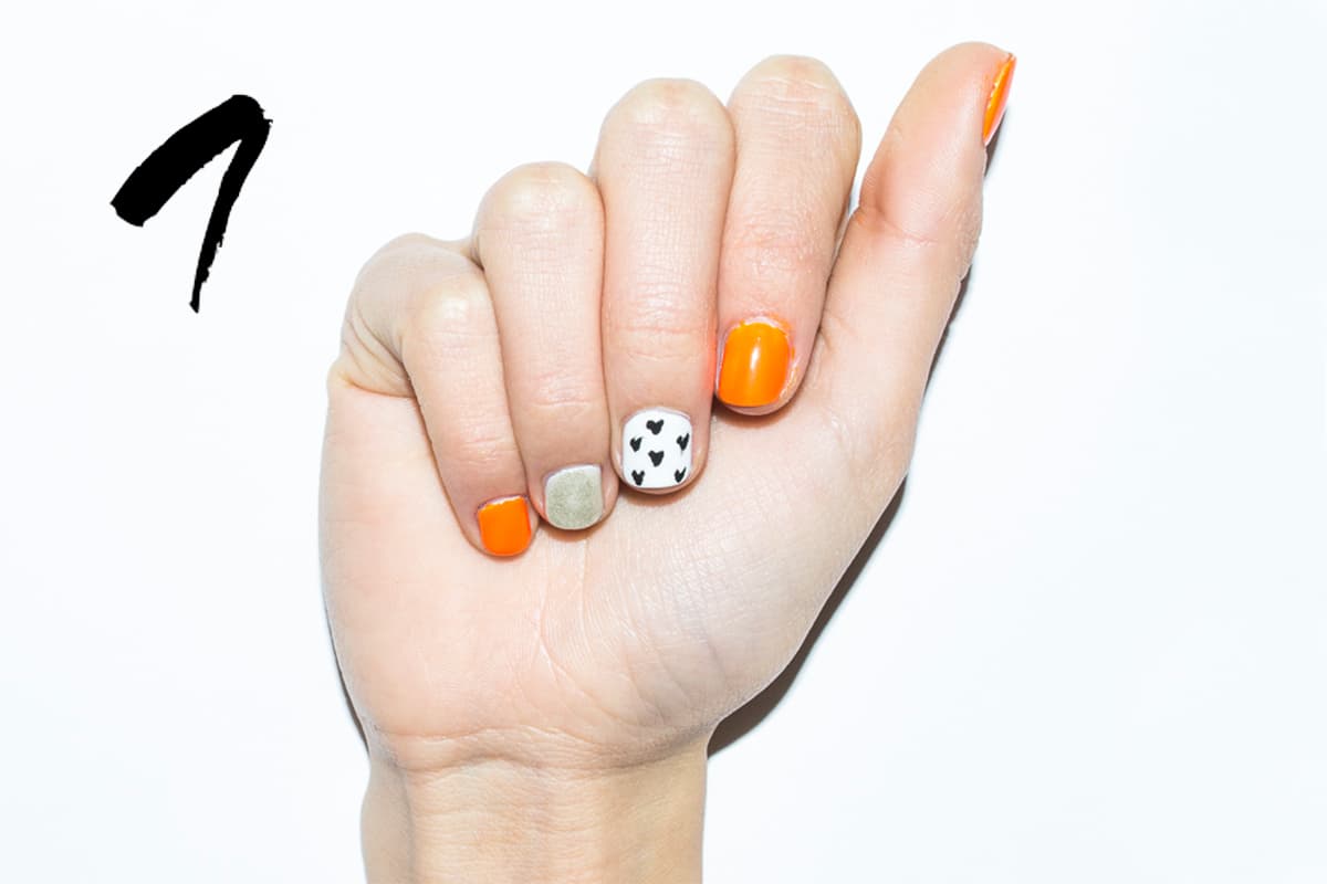 Aplica dos capas de esmalte neón en las uñas del dedo pulgar, índice y meñique, de tono dorado en la del anular y blanco en el medio. Con un puntero forma corazones en el medio.