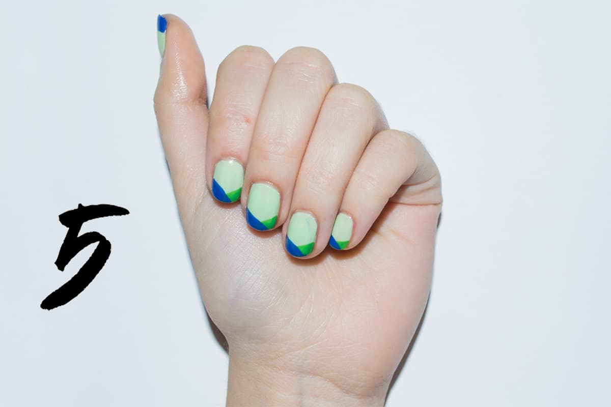 Aplica dos capas de un esmalte verde pistache. Traza en la punta una línea diagonal hacia el centro de la uña con un tono verde limón. Para el lado contrario hazlo con un tono azul eléctrico.