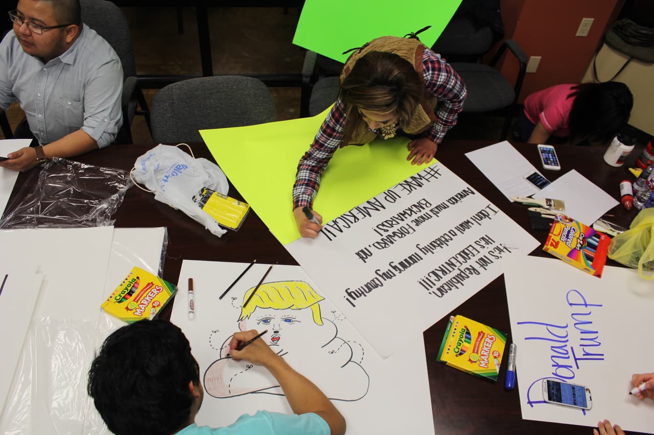 Fernando García, abajo a la izquierda, pinta su cartel de protesta contra Trump