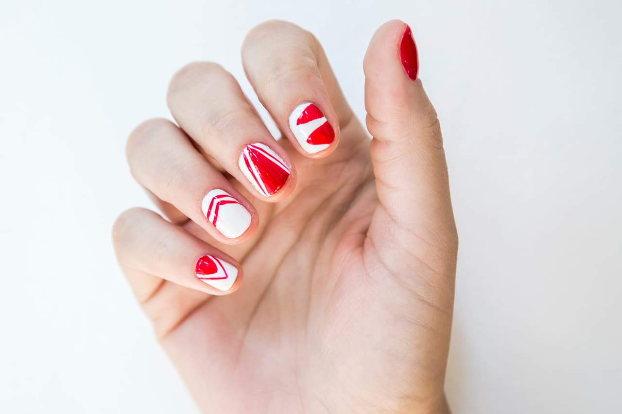 Perú: Da 2 capas de esmalte rojo en la uña del dedo pulgar y 2 capas blancas en el resto de las uñas. Con un pincel liner delgado dibuja triángulos y líneas en distintos sentidos en cada uña.