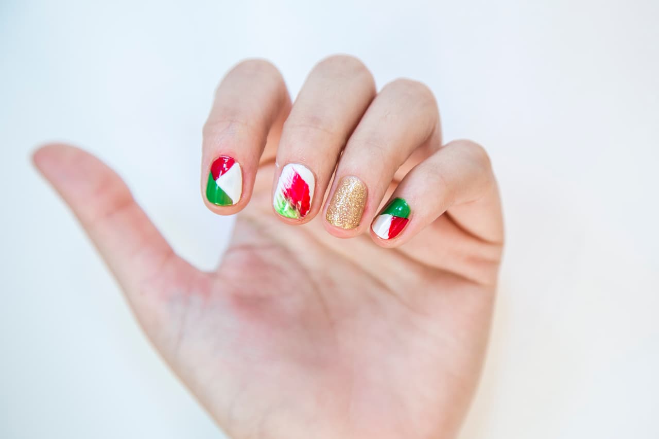 México: En la uña del dedo anular da 2 capas de barniz dorado y 2 en tono blanco en la del dedo medio. En las del dedo índice y en el meñique forma triángulos con esmaltes rojo, verde y blanco. Moja la mitad de una brocha mini abanico de esmalte rojo y la otra mitad con esmalte verde y barre de un lado al centro de la uña.