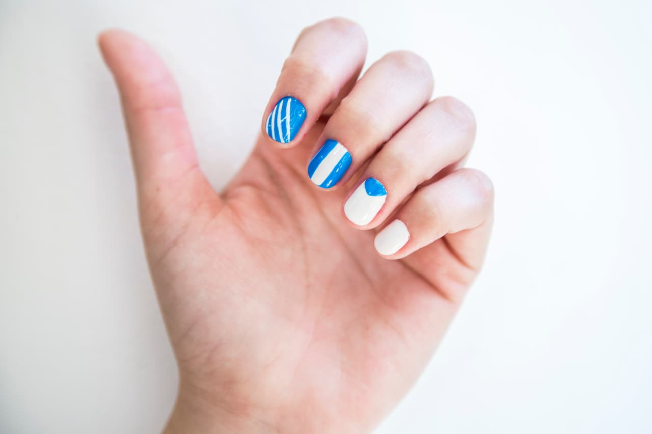 Argentina: Aplica 2 capas de barniz blanco en las uñas del meñique y anular y 2 en tono azul en el dedo medio y el índice. En la uña del dedo índice dibuja con un pincel delgado líneas diagonales blancas. En la uña del dedo índice y con un pincel más grueso haz una línea blanca en el centro de la uña del dedo medio. Con el mismo pincel dibuja un triángulo en la parte superior de la uña del dedo anular.