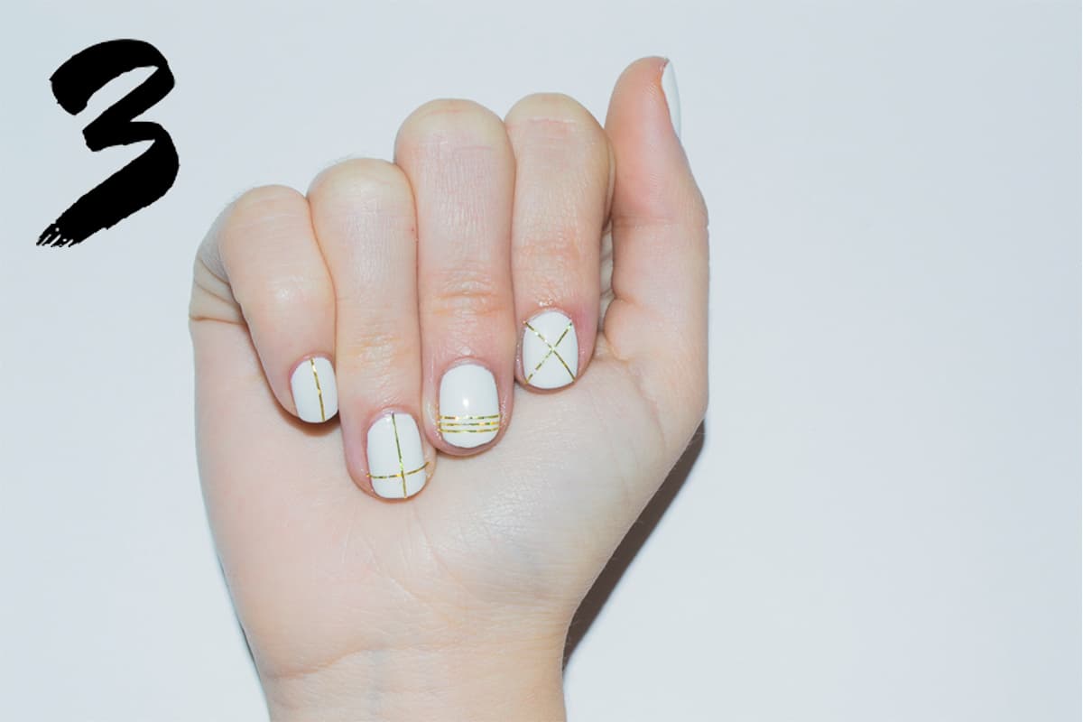 Da dos capas de esmalte blanco, ya seco, juega con cintilla dorada tornasol y traza líneas para crear diseños diferentes en cada uña. Ayúdate con unas pinzas para cortarla y para que fije bien, no olvides sellar con el brillo.