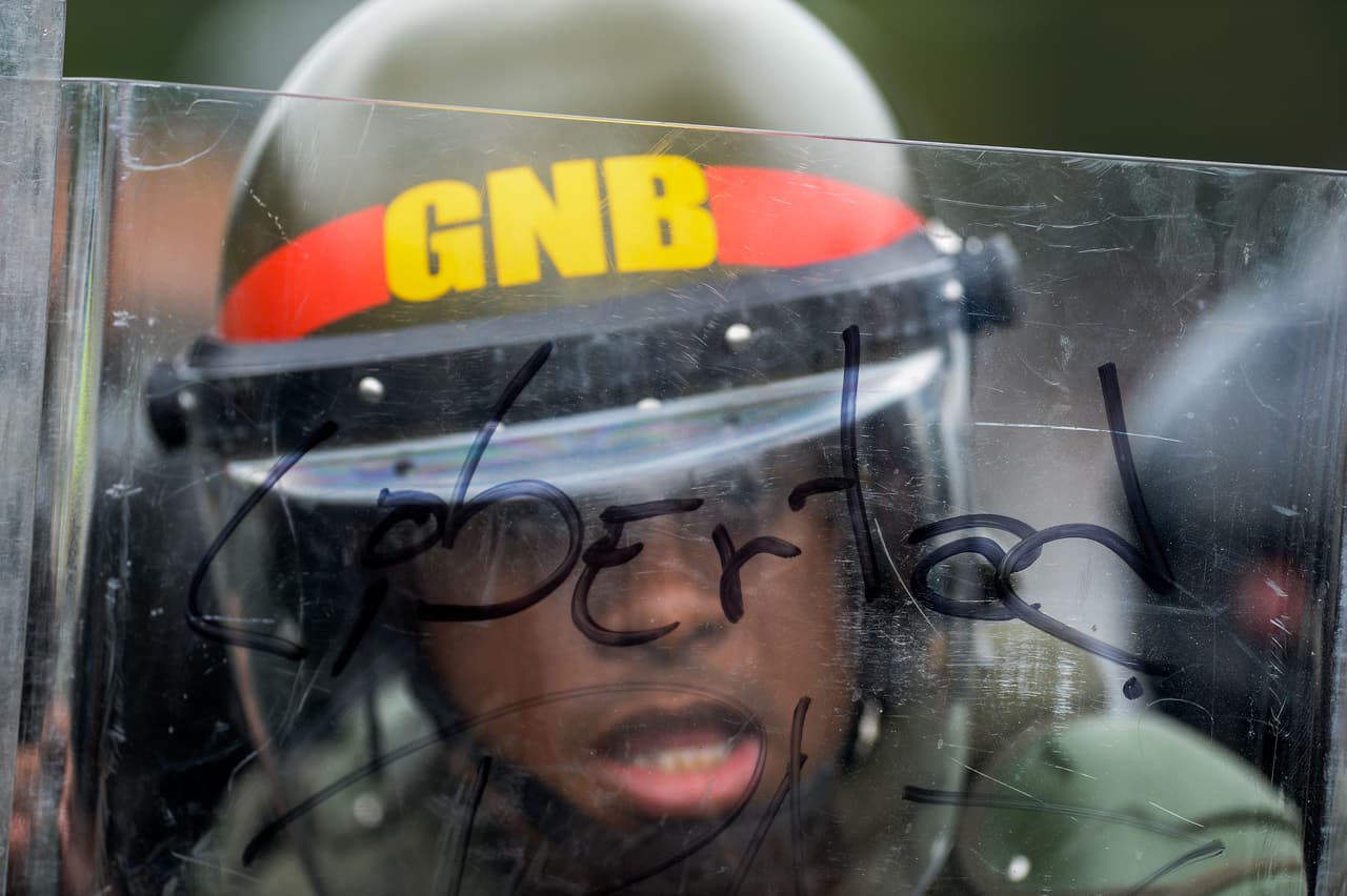 Un miembro del equipo antimotines de la Guardia Nacional se protege con un escudo transparente que tiene escrita la palabra “libertad”