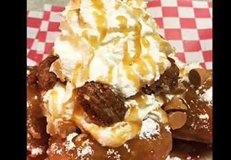 <h3 class="cms-H3-H3">Bocaditos fritos de pudín de pan de manzana, canela y canela</h3>
<br>Bocados pequeños de budín de pan tibio y mantecoso, rebozados y fritos hasta que estén dorados, mezclados con azúcar en polvo crujiente con canela y cubiertos con manzanas acarameladas tibias, salsa de caramelo, chispas de caramelo, nueces praliné y un remolino de crema batida; ¡Agrega una bola de helado de vainilla y conviértelo en un helado!