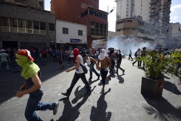 Los estudiantes desarmados salen corriendo porque les están lanzado gases lacrimogénos. Los estudiantes llevaron a cabo una manifestación pacífica contra el régimen del mandatario Nicolás Maduro el 12 de febrero de 2014. Motorizados uniformados y con sus caras cubiertas, dispararon contra los manifestantes, matando a dos estudiantes y a un oficial.