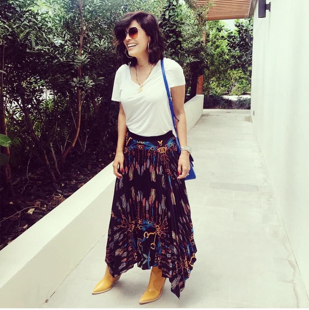 Aquí un ejemplo más de como Karla sabe llevar prendas básicas a tomar protagonismo. La falda con estampado de cadenas se encuentra en equilibrio gracias al top y la bolsa en colores lisos, mientras que las botas, joyas y lentes le dan al look un aire fashionista.