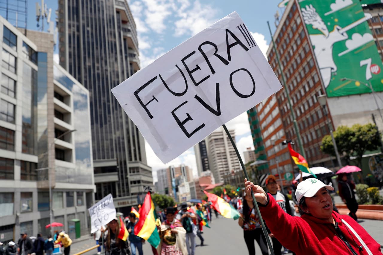 Con una pancarta que lee "Fuera Evo", una manifestante protesta en La Paz. Al final, tras el llamado de las Fuerzas Armadas para que el presidente renunciara, Morales anunció en una intervención televisada que dimitía, poniendo fin así a sus 13 años de presidencia. El comandante en jefe de las Fuerzas Armadas, Williams Kaliman, dijo que su exigencia buscaba 
<b>"la pacificación y el mantenimiento de la estabilidad</b>, por el bien de nuestra Bolivia”.
<br>
