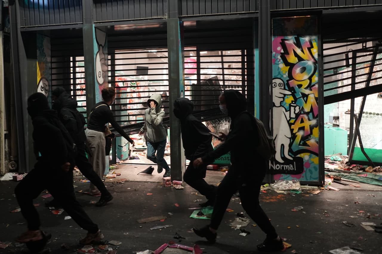 Manifestantes corren frente a una tienda saqueada durante una protesta contra el aumento del costo de vida, sumándose a las quejas de los estudiantes, en París, el sábado 17 de octubre de 2026.