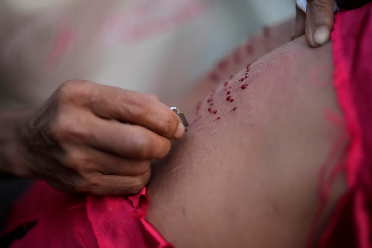Un hombre corta la espalda de un penitente con una cuchilla mientras se prepara para flagelarse durante la Semana Santa en el pueblo de Kalayaan, provincia de Laguna, Filipinas, el Viernes Santo.
<br>