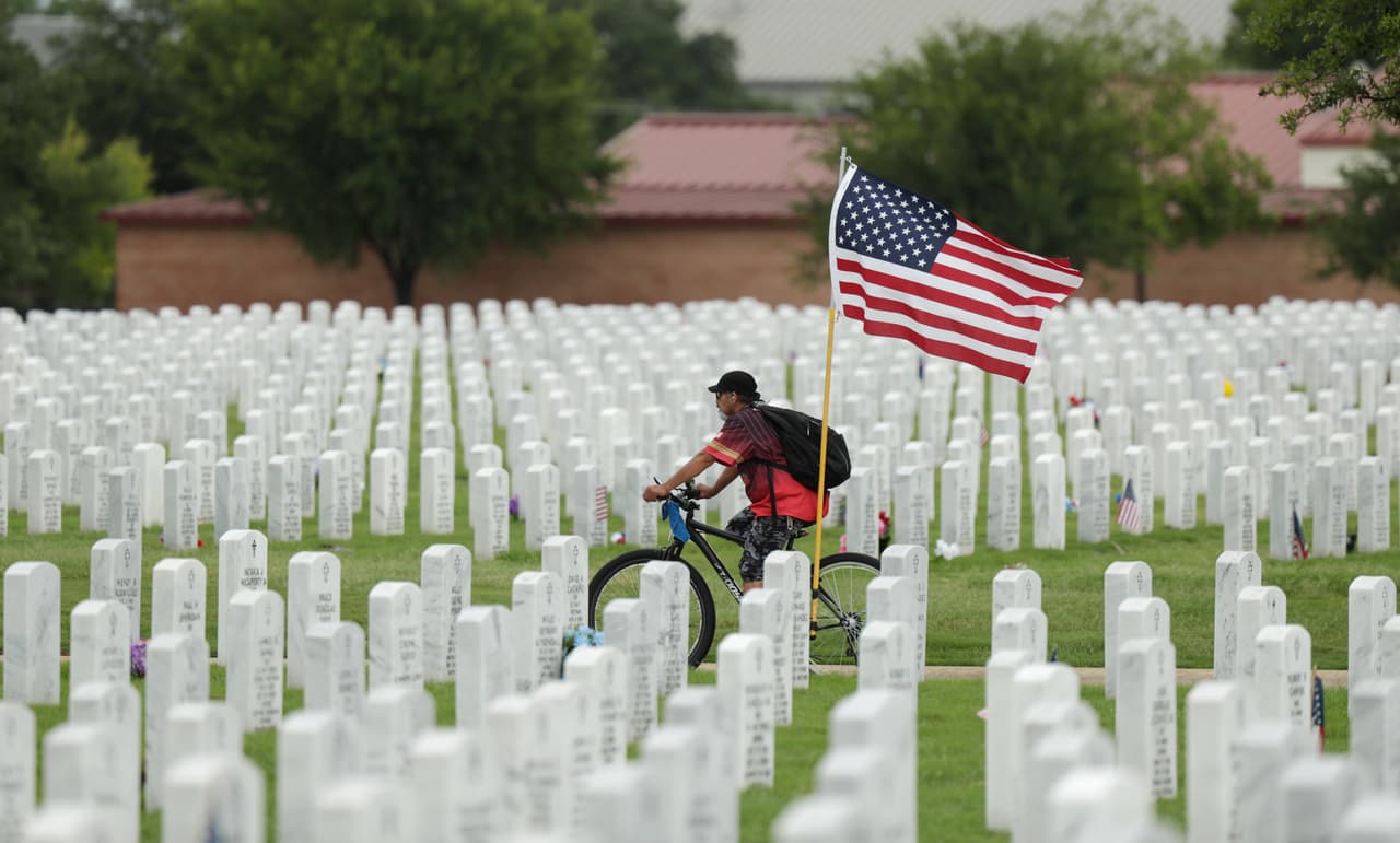 Un hombre monta su bicicleta con una gran bandera de EEUU en el Cementerio Nacional Fort Sam Houston en San Antonio.