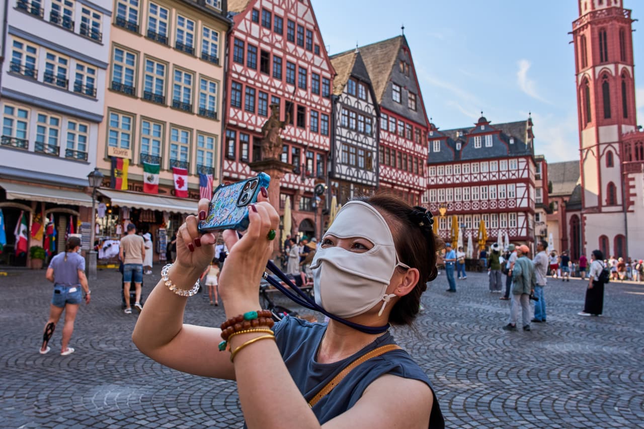 A tourist from China protects her face from the sun as she takes pictures at the Roemerberg square in Frankfurt, Germany, Saturday, June 27, 2026. (AP Photo/Michael Probst)