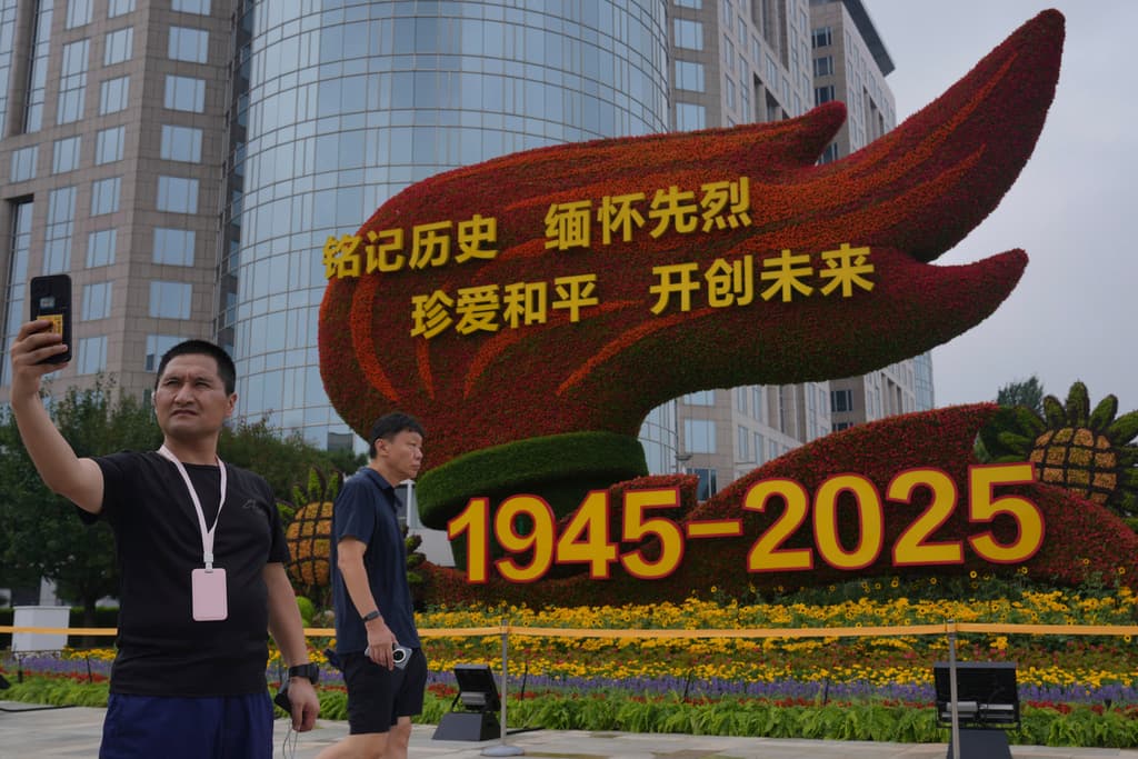 Un hombre se toma una selfie con una decoración floral que muestra mensajes propagandísticos a lo largo de la calle Chang'an, el jueves 21 de agosto de 2025 en Beijing, antes del desfile militar del 3 de septiembre que conmemorará el 80 aniversario de la rendición de Japón en la Segunda Guerra Mundial.