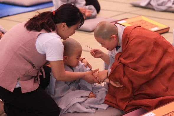 Un monje se acerca a un niño para ponerle un tipo de incienso en su brazo.