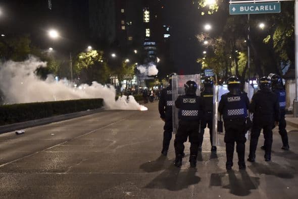 Elementos de la policía antidisturbios se resguardan de los petardos arrojados por encapuchados al término de la marcha pacífica para exigir la aparición de los 43 estudiantes de Ayotzinapa.