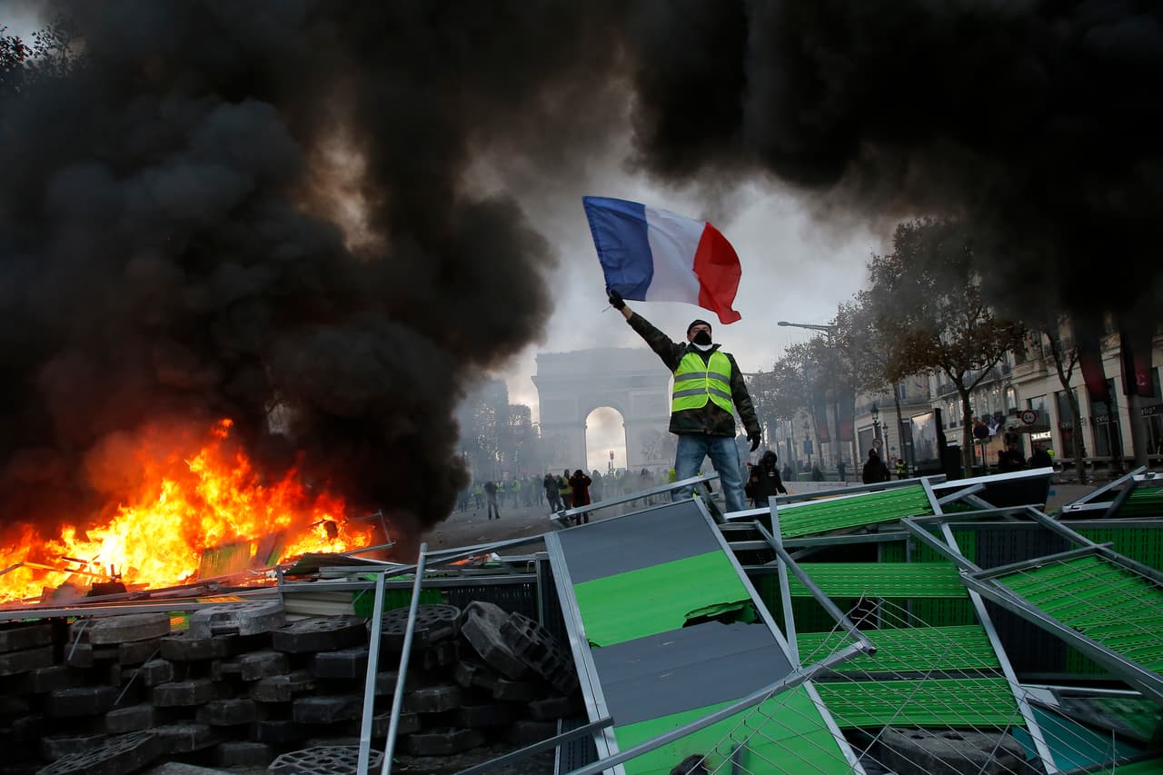 Un manifestante ondea la bandera francesa en una barricada en llamas en la avenida Champs-Elysees (los Campos Elíseos) durante una manifestación contra el aumento de los impuestos al combustible, este sábado 24 de noviembre de 2018 en París. AP/Michel Euler.