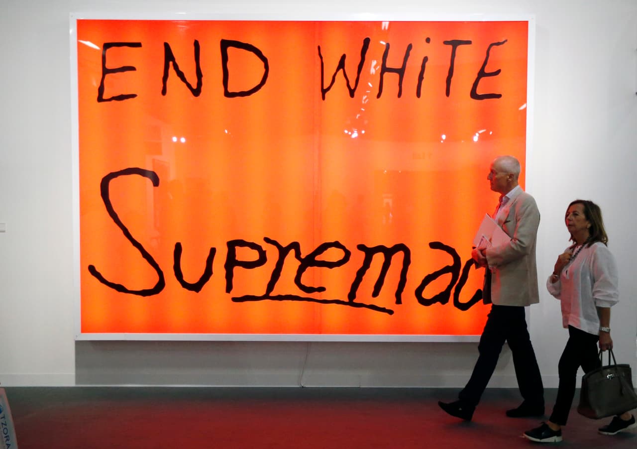 Art patrons walk by Sam Durant's "End White Supremacy" during Art Basel in Miami on November 30, 2016. Art Basel represents over 250 art galleries at the Miami Beach Convention Center and is considered one of the world's largest art festivals with art events throughout the city. / AFP / RHONA WISE / RESTRICTED TO EDITORIAL USE - MANDATORY MENTION OF THE ARTIST UPON PUBLICATION - TO ILLUSTRATE THE EVENT AS SPECIFIED IN THE CAPTION (Photo credit should read RHONA WISE/AFP/Getty Images)