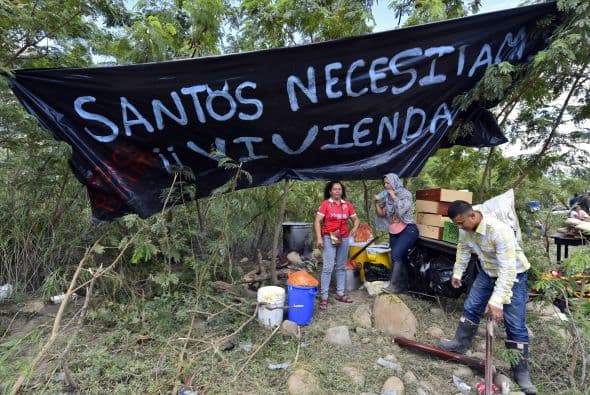 Una familia colombiana se mantiene junto a una pancarta que dice 'Santos, necesitamos vivienda'.