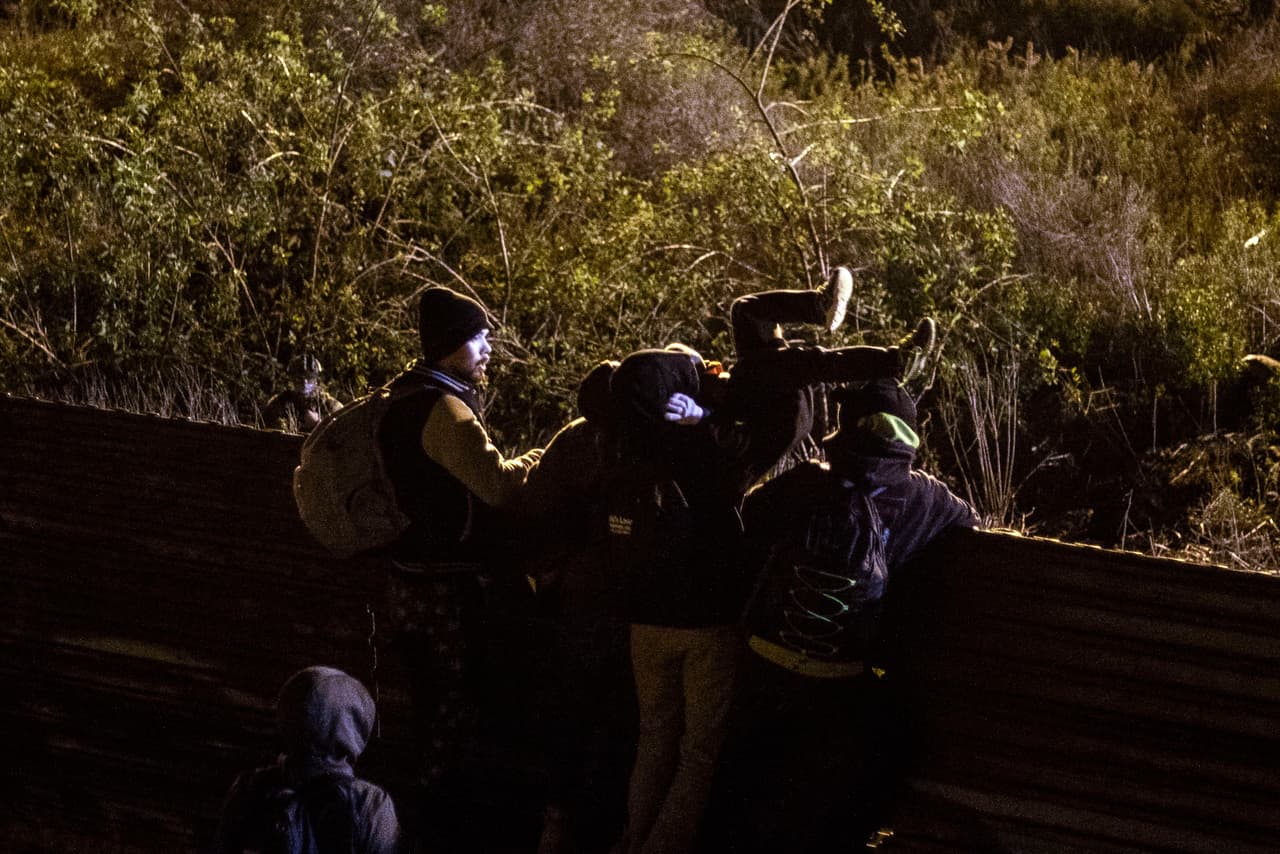 Un grupo de migrantes pasa a un niño sobre la valla fronteriza en la noche de Año Nuevo.