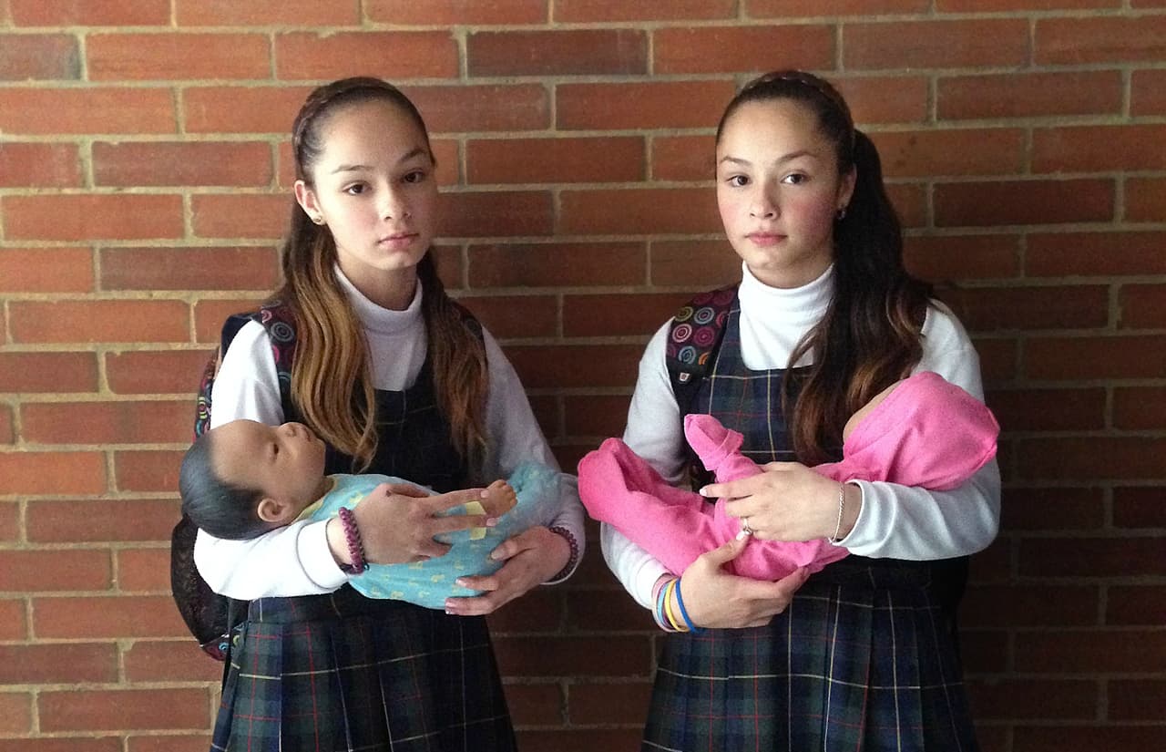 Retrato hecho por Christian Rodríguez de dos niñas en Bogotá con bebés robots que las enfrenta a la realidad de tener un bebé.