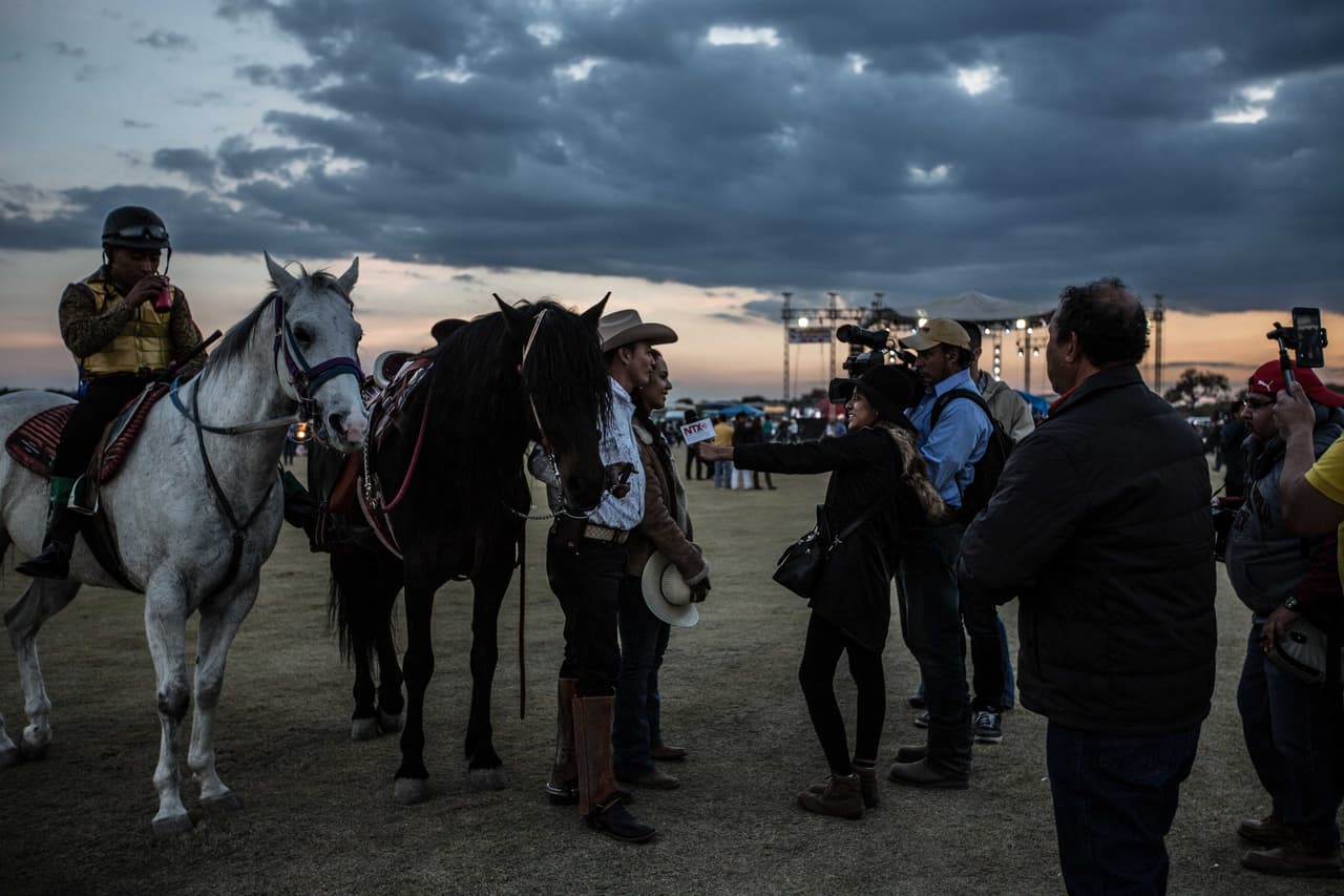 Dos periodistas de Notimex, agencia de noticias del estado mexicano, entrevistan a unos jinetes poco antes de que se supiera que un hombre resultó fallecido en la carrera de caballos apenas comenzó.