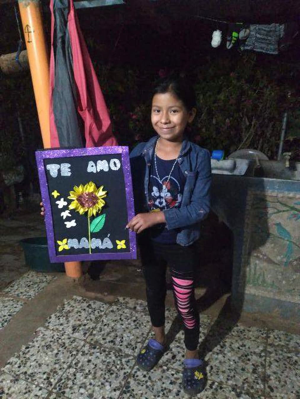 Dayana Ramírez Hernández, la hija más pequeña de Reyna, posa para una foto con un afiche para el Día de la Madre que hizo en la escuela en mayo de 2023.