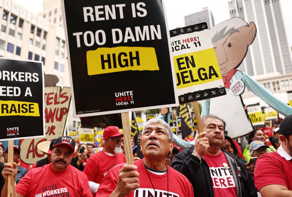 "La renta está demasiado cara", lee la pancarta del trabajador al centro. Precisamente ese es uno de los argumentos principales de los empleados en huelga de 5 hoteles reconocidos. Aseguran que con el incremento en el costo de vida, sus salarios ya no les dan para costear el pago de alquiler de un techo digno en Los Ángeles.