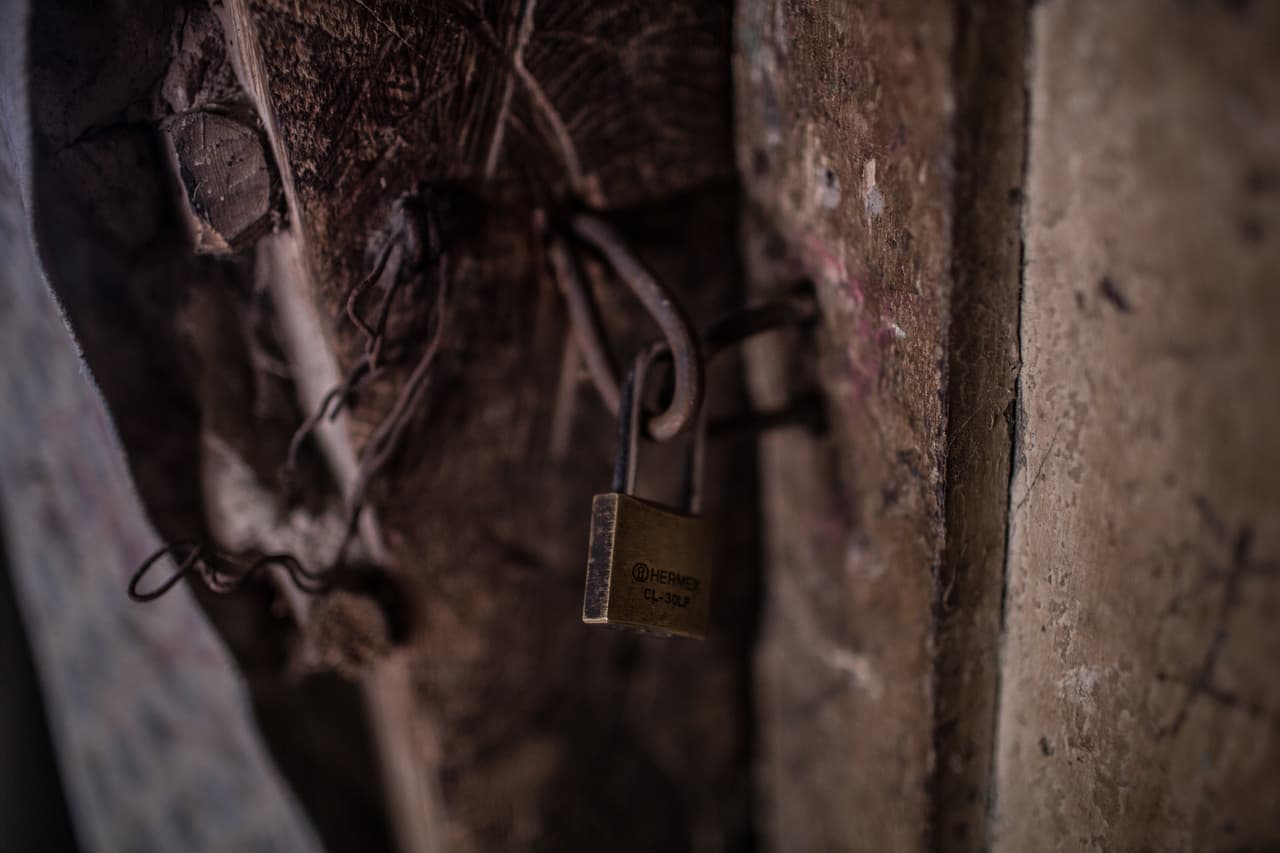 La abuela puso un candado para cerrar la puerta de la humilde casa donde la familia vivía después de que vinieran los ladrones. "Dejé mi casita con todo y hasta las cacerolas se llevaron", dice el padre de la familia. "¡Salimos así como estamos! Tres primero y los otros tres, después, con bolsitas plásticas, chiquititas, una cobijita para arropar al niño nada más".