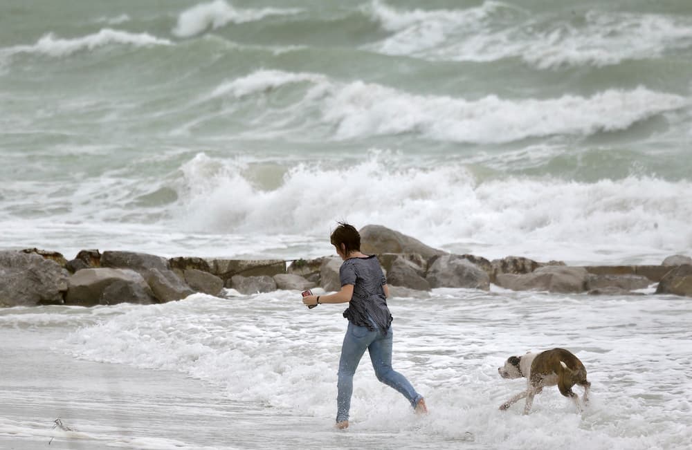 Una mujer corre con su perro en Sunset Beach, Tresure Island, donde el oleaje golpeó con fuerza en la costa