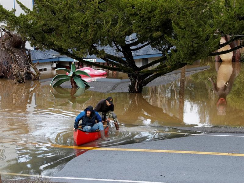 Dos personas se bajan de una canoa en Guerneville, junto a una casa inundada.
