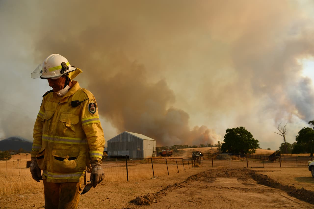 Un bombero del Servicio Rural con columnas de humo detrás este 11 de enero en Tumburumba, Australia. Ahora, Nueva Gales del Sur se está preparando para condiciones de incendio severas, con altas temperaturas y fuertes vientos pronosticados en todo el estado.
<br>