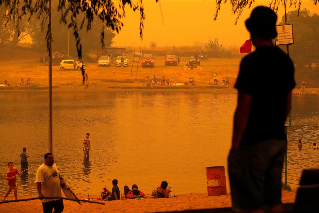 Personas se bañan en un río en Renaico, en la región de La Araucanía, consumida por varios incendios activos que intoxican el aire y hacen que el cielo se vea naranja.