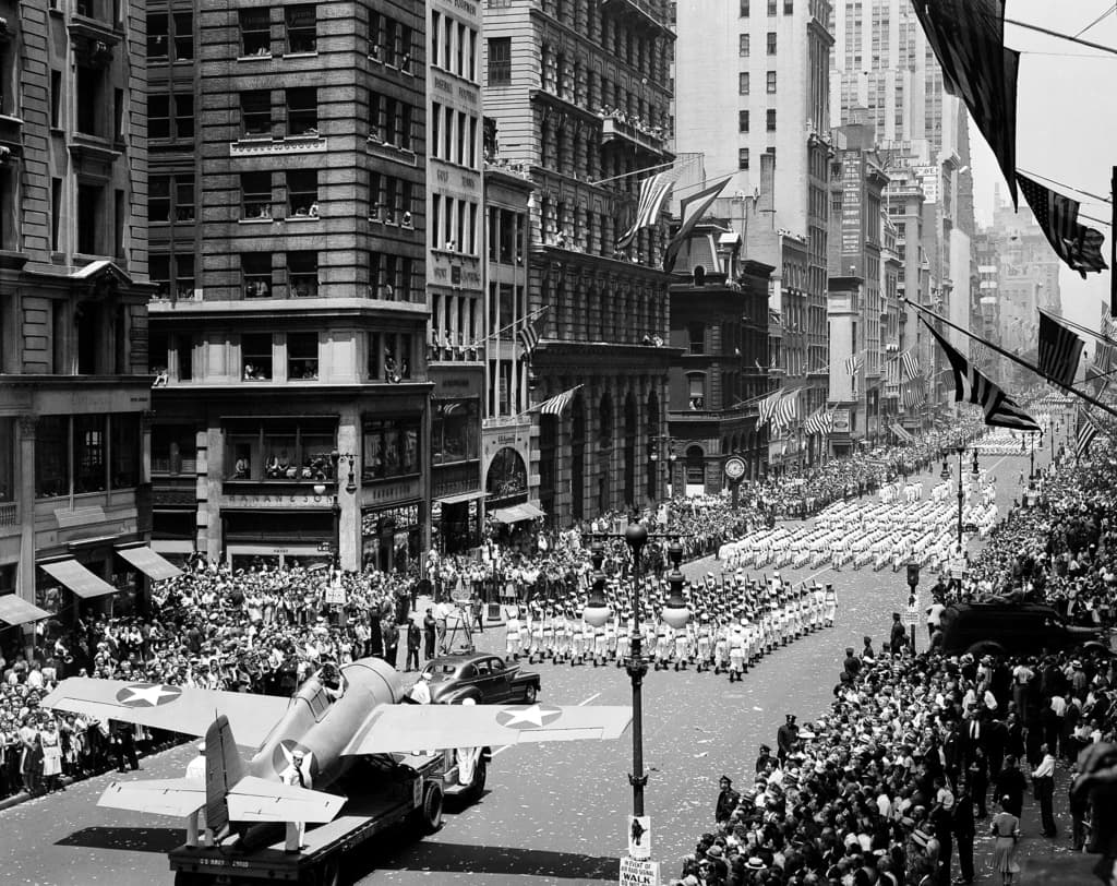 ARCHIVO - Miles de personas se congregan en las calles para vitorear a las unidades navales que marchan por la Quinta Avenida en un desfile de guerra en Nueva York, el 13 de junio de 1942. Abajo a la izquierda, un caza Grumman "Wildcat" despega desde portaaviones estadounidenses. (Foto AP, Archivo)