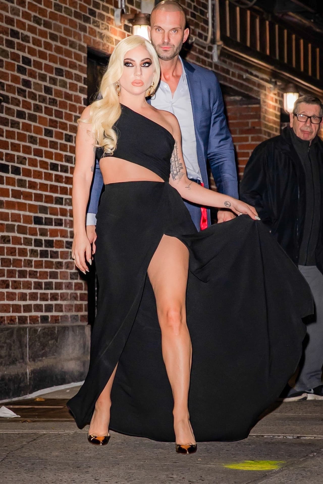 Lady Gaga lució un enorme saco brillante y debajo portó un vestido negro con abertura en el muslo de la colección primavera 2022 de Valentino. Para su look, eligió unos zapatos dorados de tacón de Gianvito Rossi.
<br>
