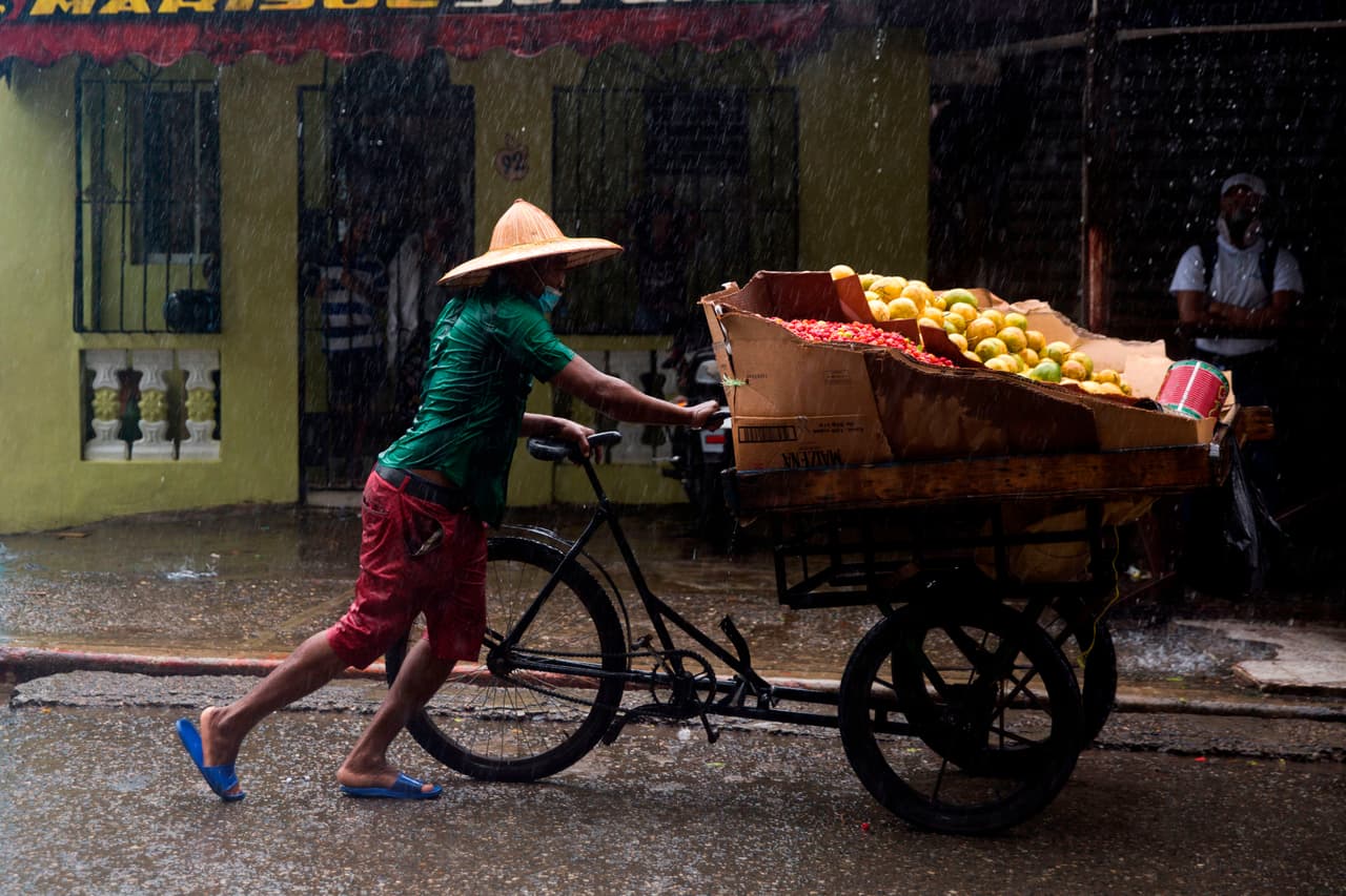 Un vendedor de mangos camina con su carro bajo una lluvia torrencial.