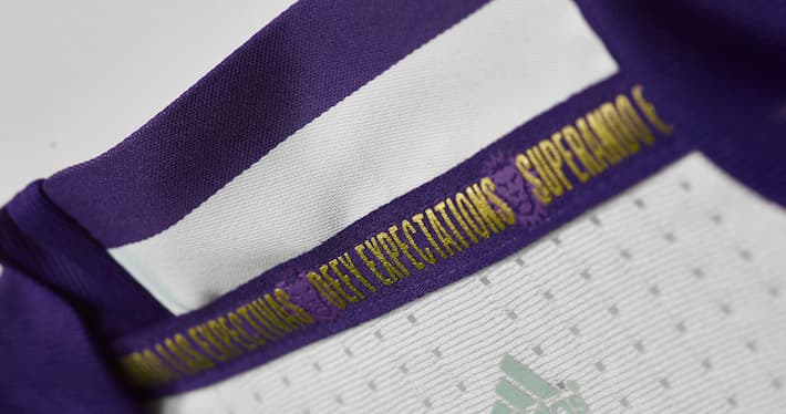 Mientras que en la parte interior se encuentra el lema del club, en inglés (Defy Expectations), en español (Superando Expectativas) y en portugués (Superando las Expectivas).