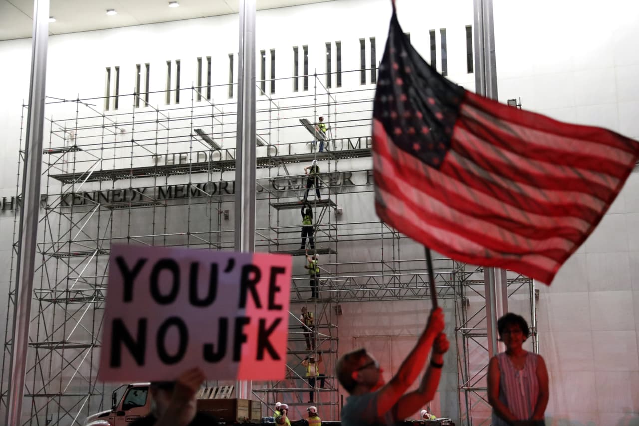 Varias personas esperan el retiro del nombre Trump y muestran cartel diciendo "No eres JFK".