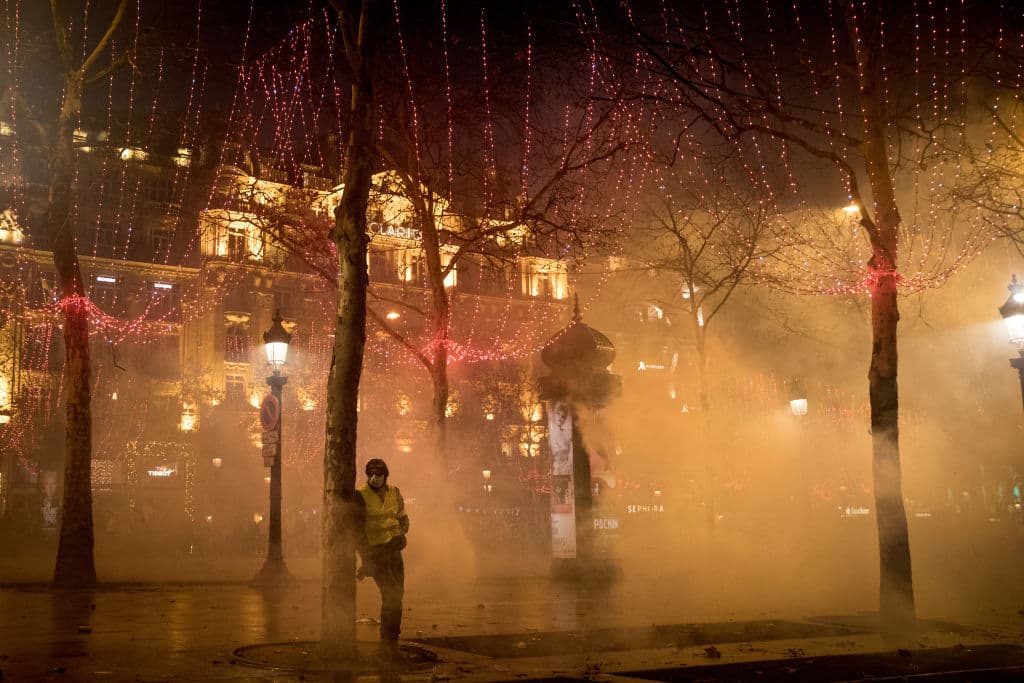 Un miembro del movimiento manifestante mira actuar a la policía entre la bruma provocada por el gas lacrimógeno.