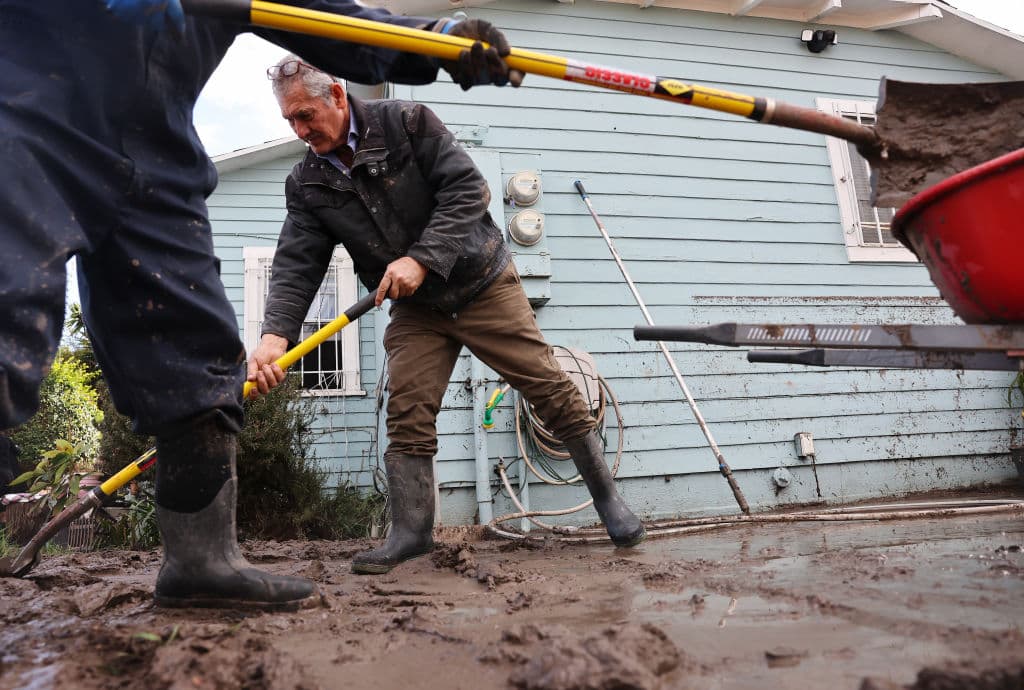 Este hombre barre la capa de lodo que quedó alrededor de su casa en San Diego debido a las inundaciones causadas por las fuertes lluvias.