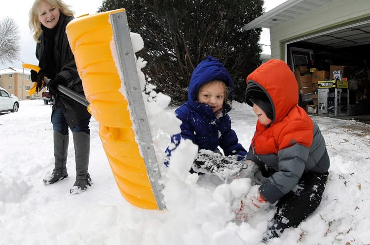 Dos niñas juegan en la nieve mientras su tía trata de limpiar la entrada de la casa, en Bismarck, North Dakota