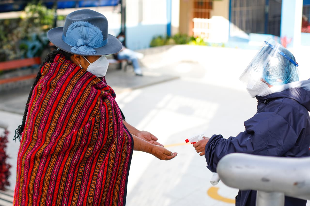 En Perú, los votantes acudieron a las urnas para elegir entre
<b><a href="https://www.univision.com/noticias/america-latina/quienes-son-los-favoritos-en-las-elecciones-presidenciales-en-peru">18 candidatos, </a> lo practicamente garantizaba una segunda vuelta. </b>En la imagen, una representante de la Oficina Nacional de Procesos Electorales (ONPE) rocía alcohol en las manos de una votante a la entrada de un centro.