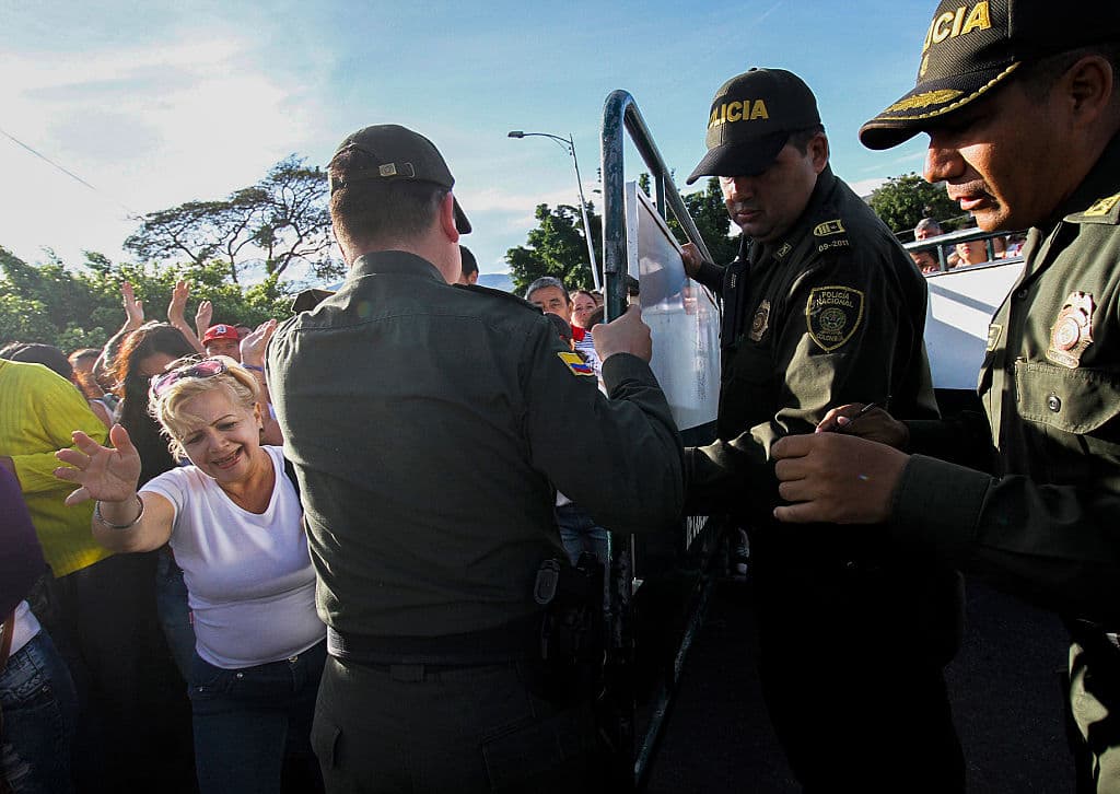 Funcionarios de la policía colombiana (derecha) y venezolana (izquierda) levantan la valla para abrir la frontera mientras los venezolanos cruzan el puente Simón Bolívar de San Antonio del Táchira, Venezuela, hacia Cúcuta, Colombia, el 10 de julio de 2016. Fue la primera vez que las mujeres vestidas de blanco lideraron la avanzada hacia Colombia, a pesar de la política de "puertas cerradas". Foto: SCHNEYDER MENDOZA/AFP/Getty Images.