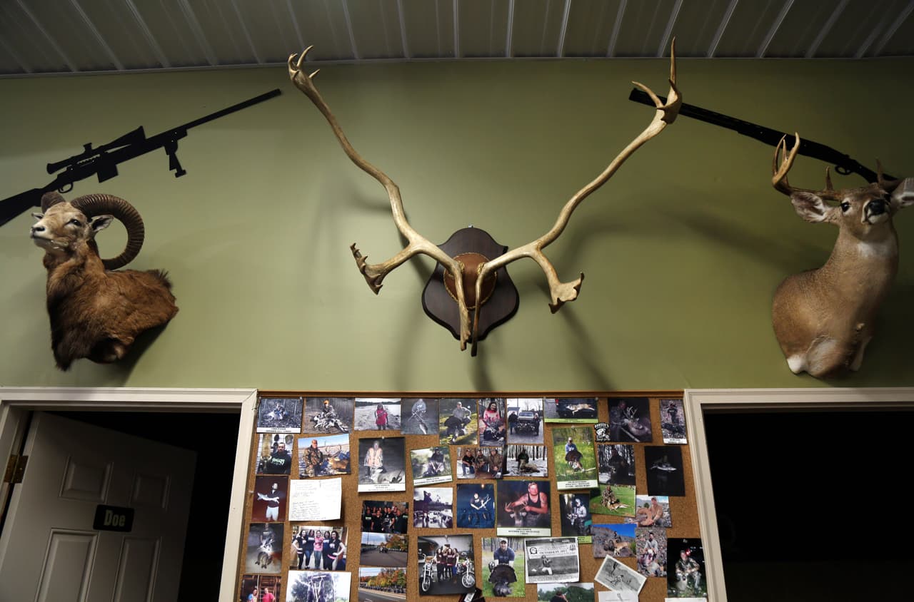 Un rifle moderno, izquierda, un rifle tradicional, derecha, un busto de un carnero, y un busto y unas astas de venado decoran una pared de la tienda de armas Banger's.