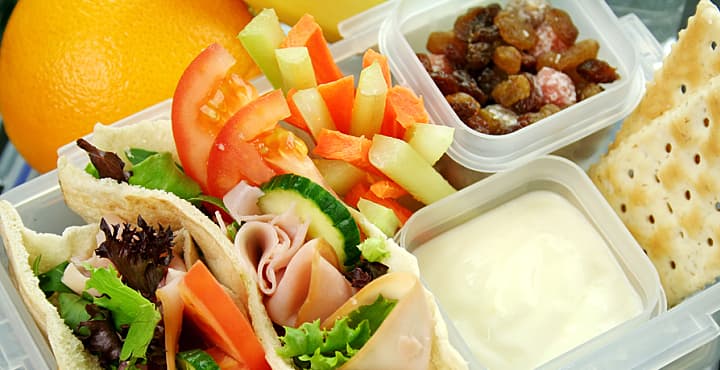 Healthy kid's lunch box made up of pita bread ham and salad fresh fruit sultanas and drinking water.